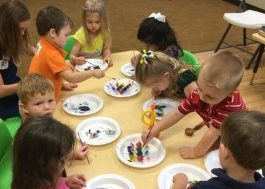 group of pre-school children sitting/standing around a table and painting