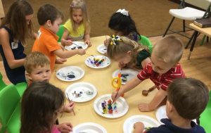 group of pre-school children sitting/standing around a table and painting